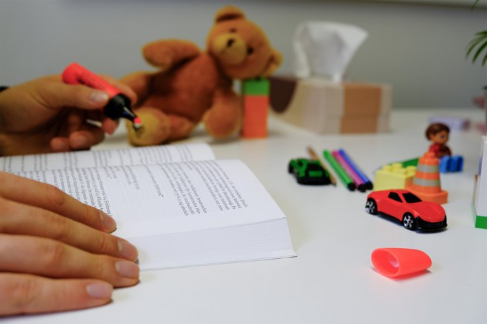 A person’s hands highlighting text in a book. A toy lies next to it.