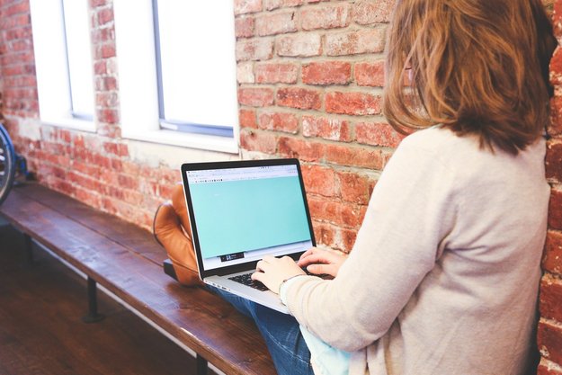 Eine Frau sitz am Fenster und schreibt auf dem Laptop