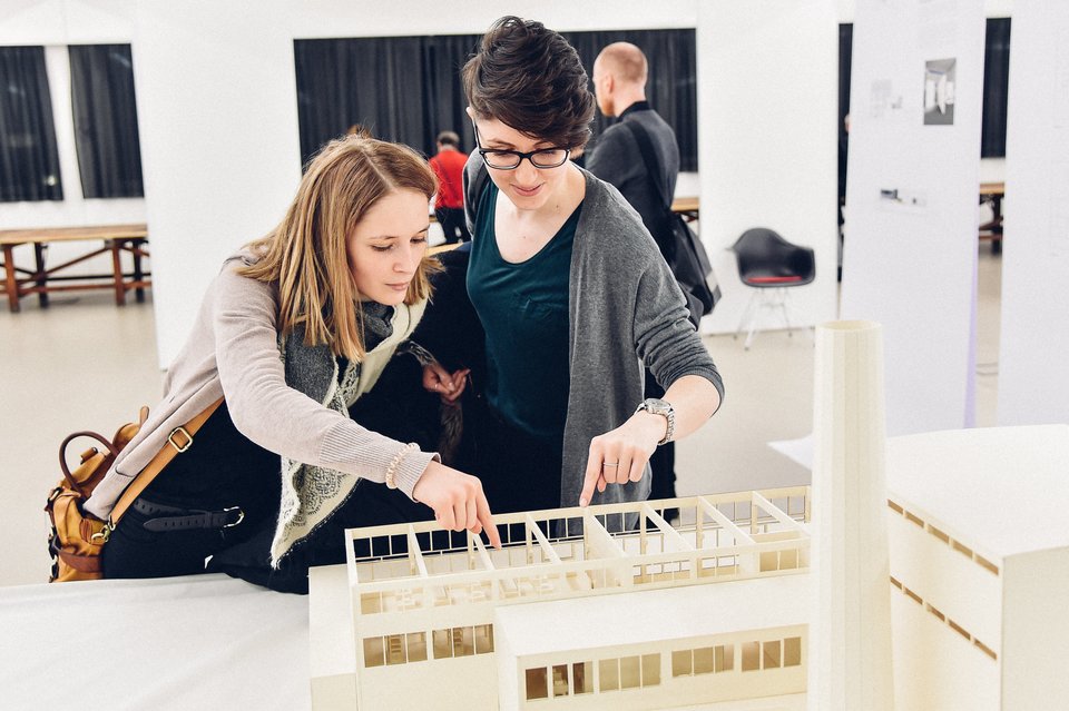 Zwei Studierende betrachten ein Architekturmodell bei der Ausstellung Pausa