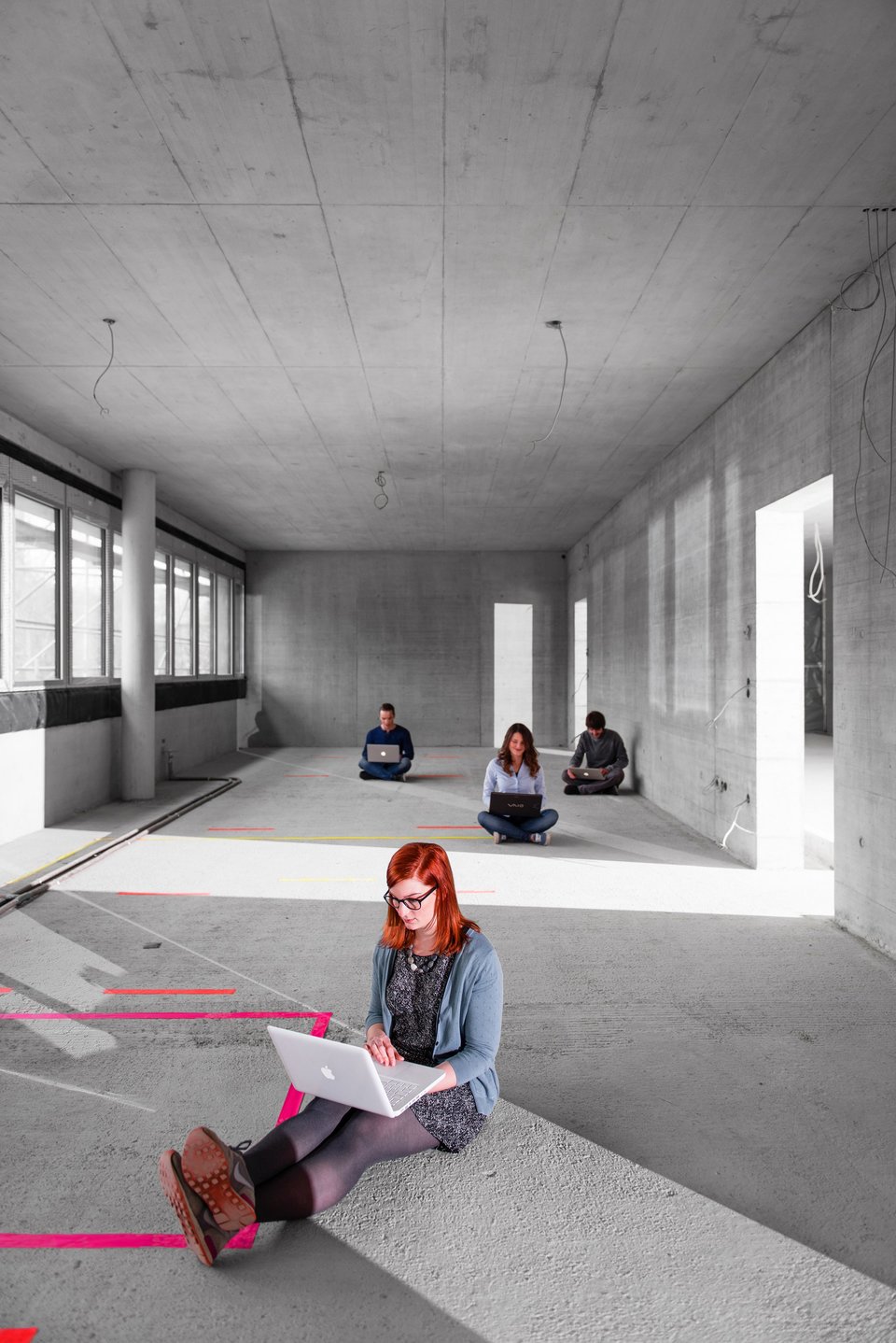 Studierende, die auf dem Boden sitzen, arbeiten an Laptops im Rohbau eines Gebäudes