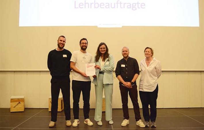 Fünf Personen auf Podium bei Preisverleihung mit Urkundenübergabe