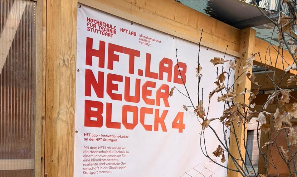Fassadenausschnitt eines Holzgebäudes auf dem ein Plakat mit Aufschrift HFT.Lab Neuer Block 4 zu sehen ist.