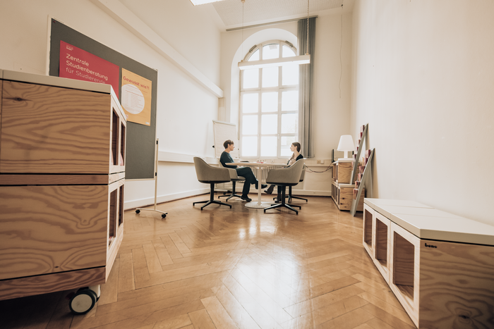 Blick in einen Raum, im hinteren Bereich sitzen eine Studentin und eine Beraterin am Tisch