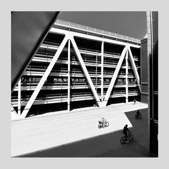 Schwarzweiß Architekturfotografie einer Straßenszene mit Fahrradfahrern und Parkhaus im Hintergrund