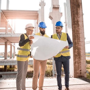 Drei Personen betrachten einen Bauplan auf einer Baustelle