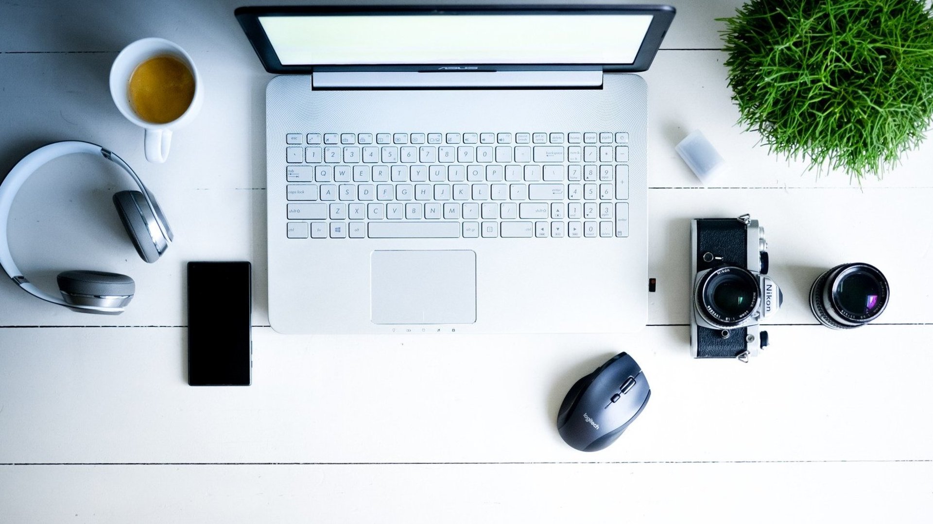 Arbeitsplatz mit Laptop, Handy, Kopfhörer, Fotoapparat, Kaffeetasse